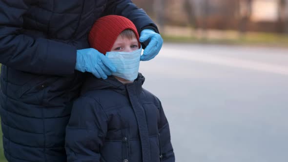 Mother adjusts the protective medical mask for her young son on the street of a European city. 