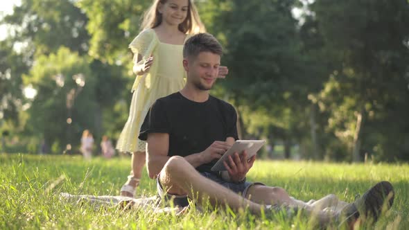 Wide Shot Relaxed Man Surfing Internet on Tablet As Cute Little Girl Covering Eyes with Hands alt