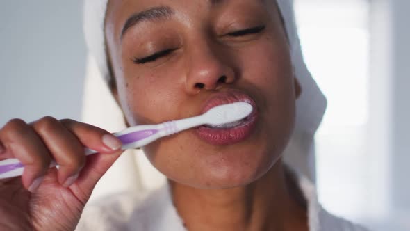 Portrait of african american woman in bathrobe brushing her teeth in the bathroom alt