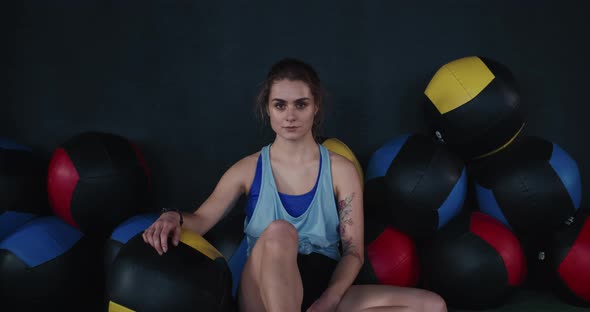 Portrait of Young Attractive Athlete Woman Sitting on Gym Floor Near Cross Fit Balls Looking at alt