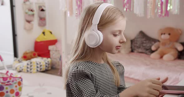 The 7Yearold Girl in the Children's Room with Headphones and Using Smartphone alt