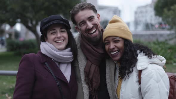Three Happy Multiracial Friends in Winter Clothes Standing Together in City alt