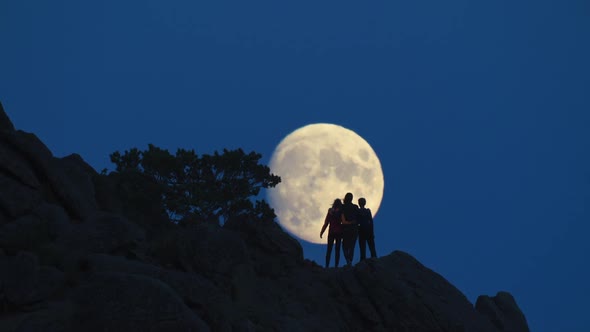 Silhouette of Family of Three People on Rocks Opposite Huge Moon