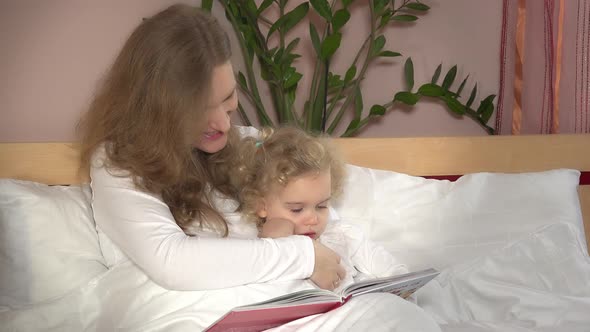 Woman and Baby Girl Reading Book. Mother and Her Little Cute Child on Bed