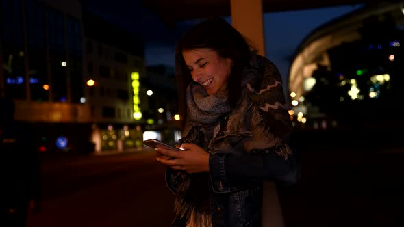 Happy young woman using smartphone at night alt