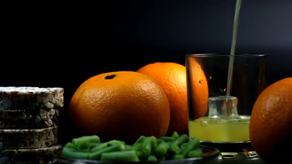 Orange, Oranges, Beans, And Bread Rolls Are Poured Into A Glass On A Black Background