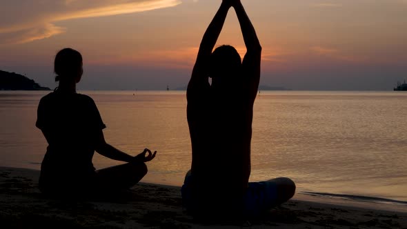 Man and Woman's Silhouette Sits in Lotus Position, Meditating and Does Yoga Excercises on Sunset