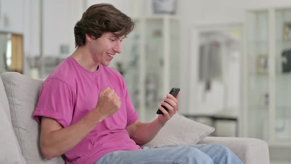 Ambitious Casual Young Man Celebrating Success on Smart Phone alt