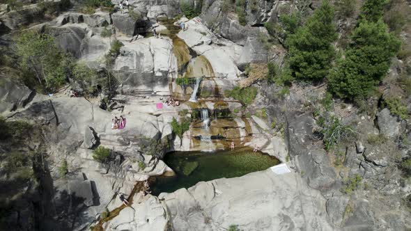 People relaxing on rocks next to natural pool at Cascatas de Fecha de Barjas in Peneda-Geres Park
