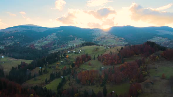 Aerial View of Distant Village with Small Shepherd Houses on Wide Hill Meadows Between Autumn Forest alt
