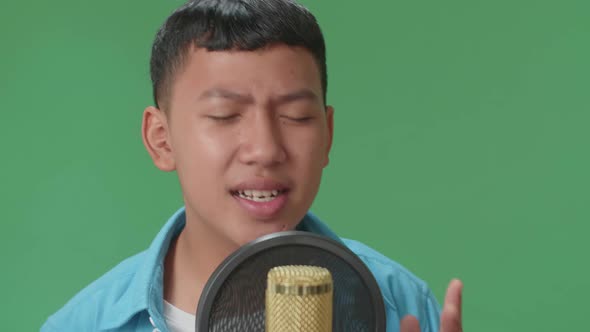Young Asian Boy Singing Into Microphone In Green Screen Studio alt