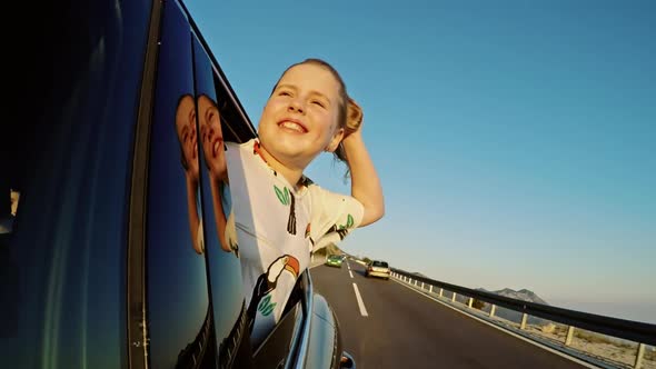 A Blonde Young Girl with Her Head Out the Window Enjoying a Scenic Drive Through the Mountain alt