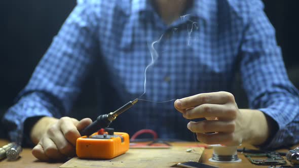 Male Engineer Solders Metal Wire During Working Day at Table in Service Center. Irrl alt