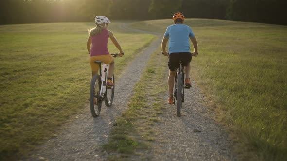 Following Couple Cycling on Gravel Path Through Grassland alt