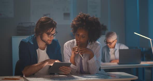 Multiracial Engineer Team Working in Dark Office with Tablet Pc and Blueprint alt