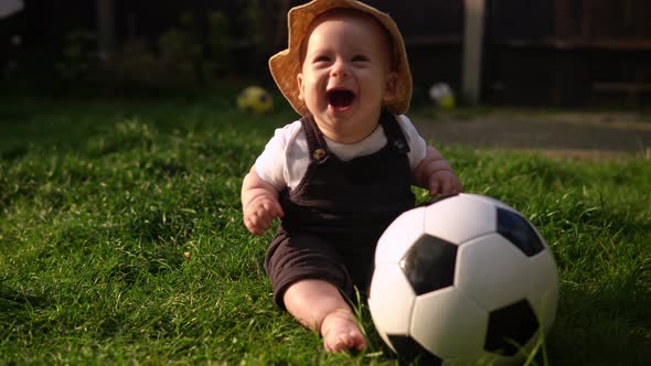 Happy Baby Sitting With Soccer Black White Classic Ball On Green Grass