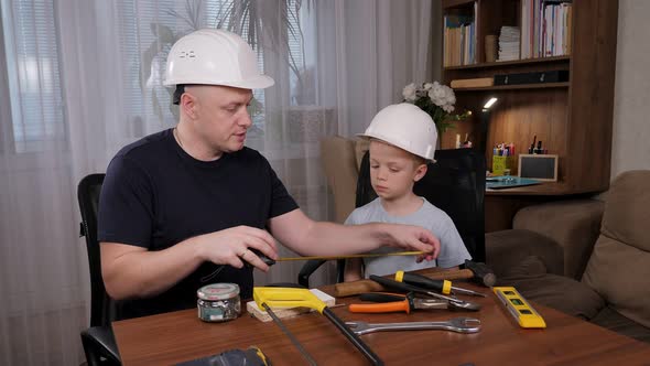 Handsome Bald Man Showing Instruments to His Son While Sitting at the Table alt