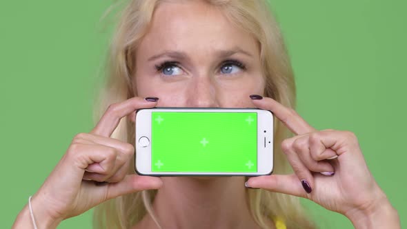 Young Happy Beautiful Blonde Woman Thinking While Showing Phone