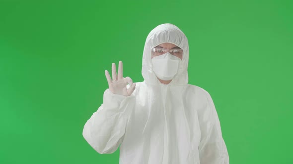 Man Wear Protective Uniform PPE, Medical Face Mask And Showing Hand Ok Sign In Green Screen Studio alt