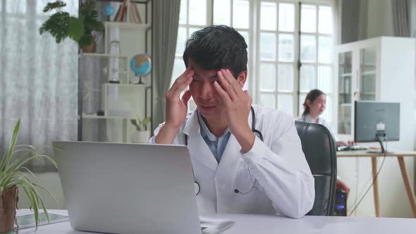 Young Asian Man Doctor Is Using Laptop Computer And Headache In Workplace. Medical Concept alt