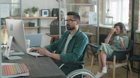 Middle Eastern Businessman Sitting in Wheelchair and Working on Computer alt