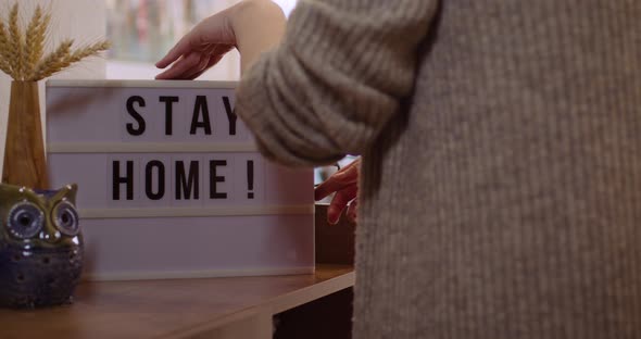 Woman walks in and Switches on Decorative Lightbox Written Stay Home in Comfy and Cozy Home alt