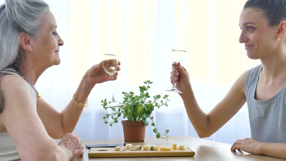 Female Portrait of Adult Daughter and Senior Mother Talking and Drinking Champagne at Home Sitting alt