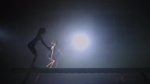 Three Female Sporty Persons are Performing Jump on Balance Beam Training Together in Dark Sports alt