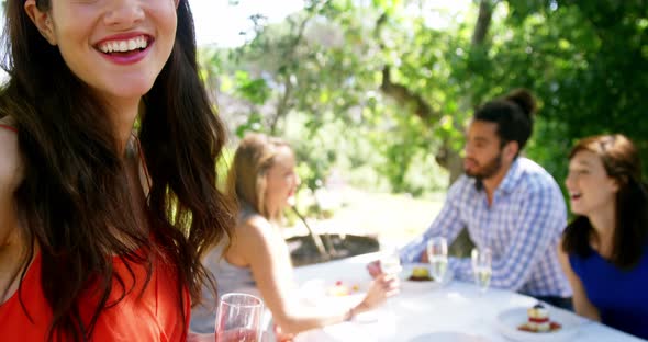 Portrait of woman standing with champagne glass while friends interacting in background alt