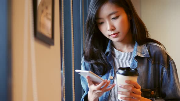 Businesswoman using smartphone beside a window at the office.