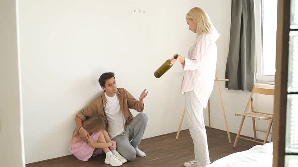 Young Mother with an Empty Bottle Against the Background of a Depressive Husband and Daughter