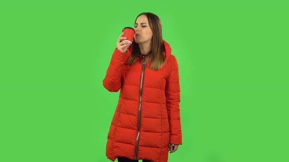 Lovely Girl in a Red Down Jacket Is Drinking Unpalatable Coffee and Is Disgusted. Green Screen alt