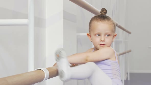 Adorable Little Ballerina Girl Putting Her Leg on Ballet Bar for Stretching