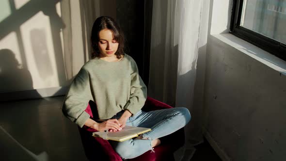 Beautiful Woman Sitting Near Window and Writing Things at the Sunset alt
