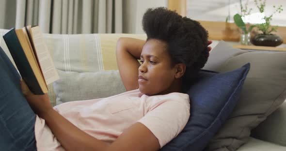 Happy african american woman sitting on sofa, reading book alt