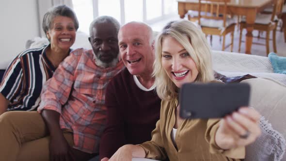 Two diverse senior couples sitting on a couch using a smartphone and taking a selfie alt
