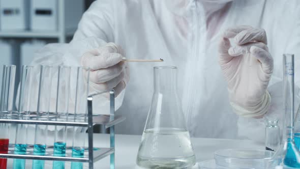 Professional Chemist Wearing Protective Uniform with Gloves Adding Pink Powder and Mixing Solution alt