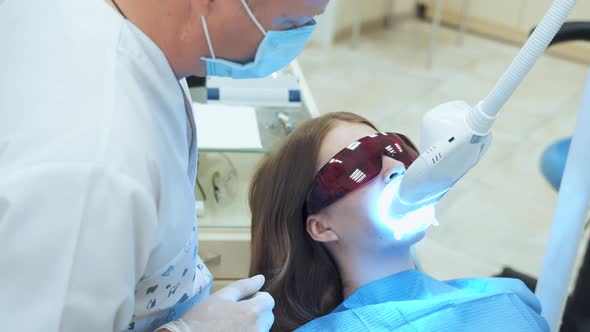 Dentist doctor turns off the device for laser teeth whitening. alt