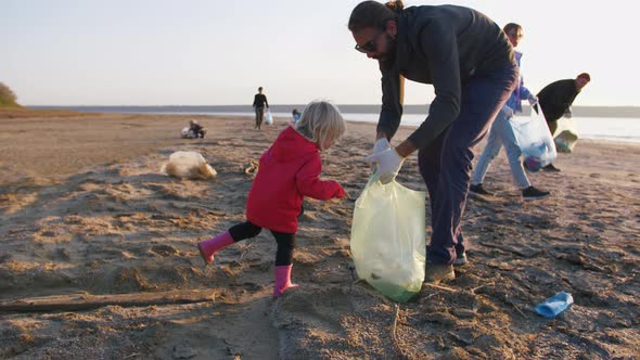 Little Girl Helps Her Parents to Clean Up Area of Dirty Beach with Garbage Bags Slow Motion alt