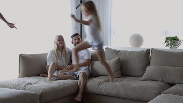 Children Playing Running Around the House While Young Parents Relaxing at Home on Sofa