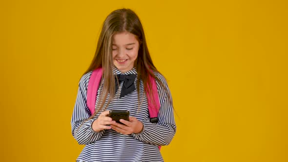Cute girl is typing text on the phone on a yellow background. technology and communication concept