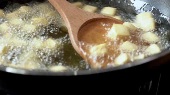 Fried tofu cubes being removed with wooden spoon from boiling hot cooking oil