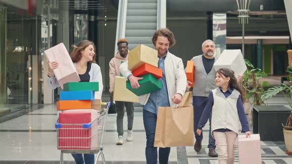 Group of Satisfied Customers Carrying Paper Bags With Purchases and Walking Along Shopping Mall alt