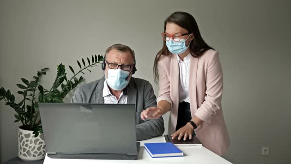 Office Work During the Covid-19 Epidemic. Young Employee Helps a Manager Solve Problems. alt
