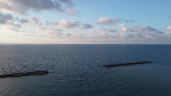 Aerial mesmerizing shot of wave blockers in the sea, light clouds and clear horizon alt