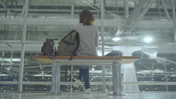 Asian woman looking around sitting on chair in terminal hall while waiting her flight