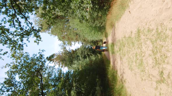 Vertical Video of a Young Blonde Woman Walking with Two Dogs down a Forest path alt