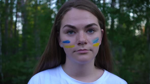 Headshot of Young Brunette Ukrainian Woman with Blue and Yellow Strips Painted on Face Looking at alt