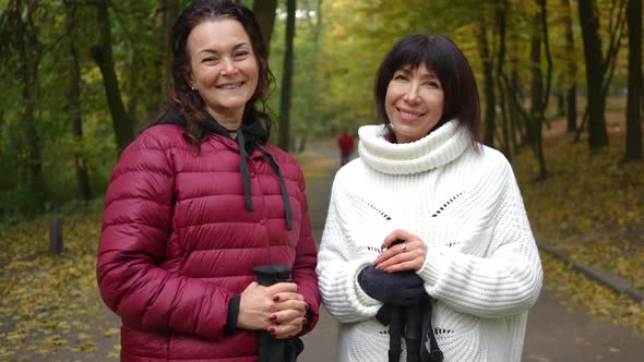 Medium Shot Portrait of Two Happy Mature Women Looking at Camera Smiling Standing on Alley in Autumn alt