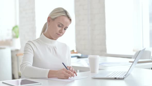 Upset Young Businesswoman Writing Documents on Office Desk alt